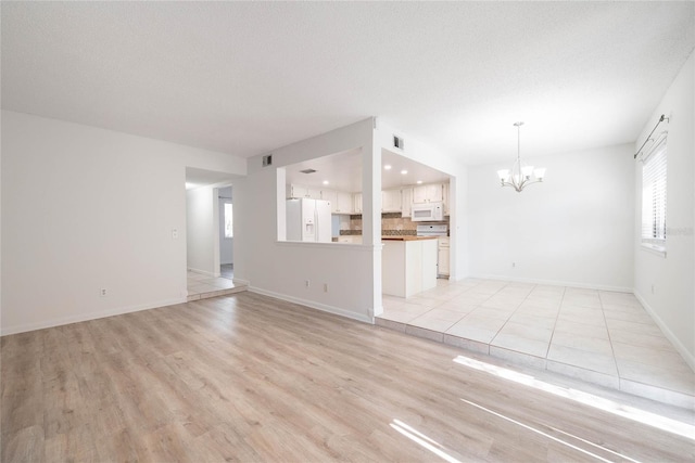 unfurnished living room featuring baseboards, visible vents, light wood-style floors, a textured ceiling, and a chandelier