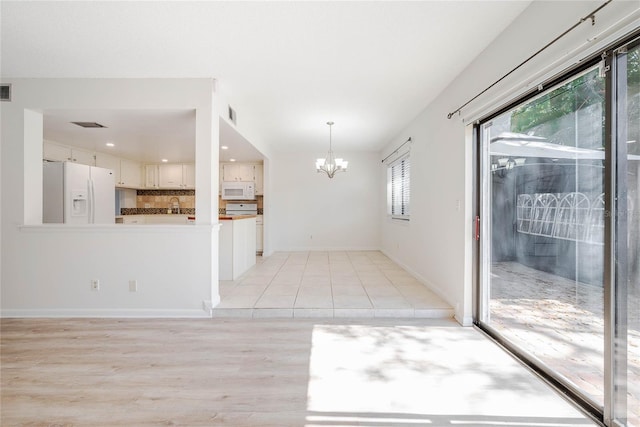 unfurnished dining area with visible vents, baseboards, light wood finished floors, an inviting chandelier, and a sink