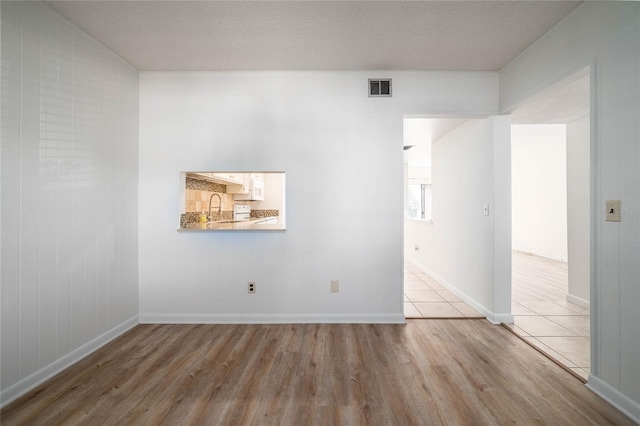 unfurnished room featuring wood finished floors, baseboards, visible vents, a sink, and a textured ceiling