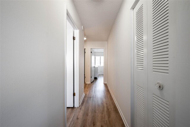 hall with a textured ceiling, baseboards, and wood finished floors