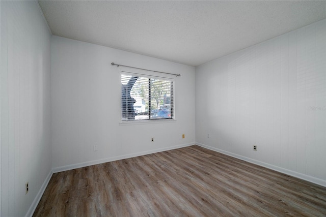 empty room featuring a textured ceiling, baseboards, and wood finished floors