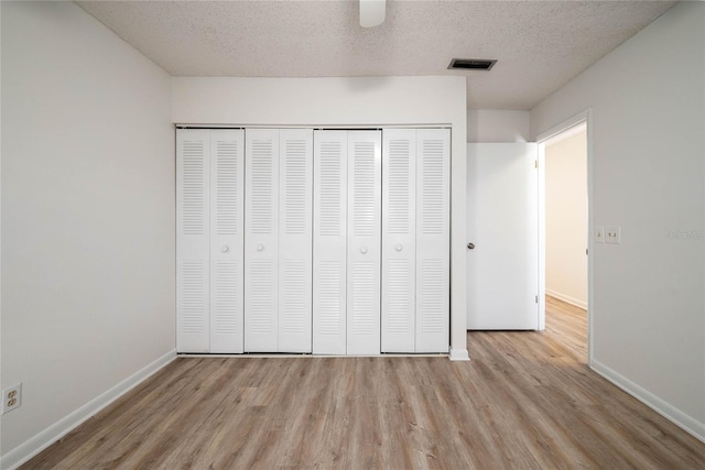 unfurnished bedroom with visible vents, a textured ceiling, a closet, and light wood finished floors