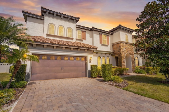 mediterranean / spanish house featuring stucco siding, an attached garage, a tile roof, and decorative driveway