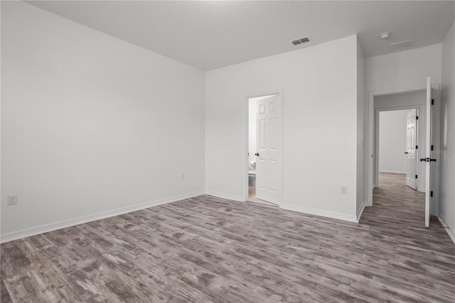 spare room with wood finished floors, visible vents, and baseboards