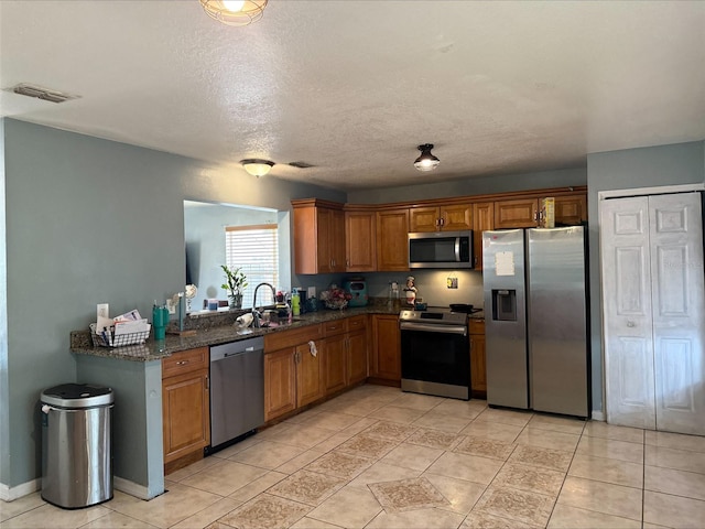 kitchen with visible vents, brown cabinets, a sink, dark stone countertops, and stainless steel appliances