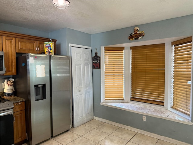 kitchen with baseboards, appliances with stainless steel finishes, light tile patterned flooring, brown cabinetry, and a textured ceiling