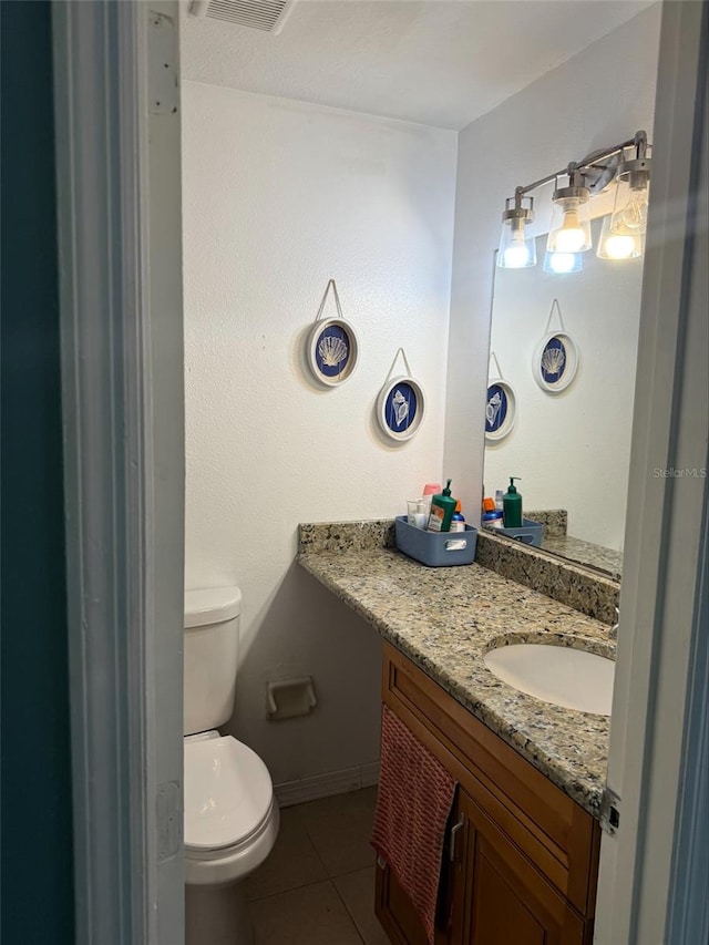 half bathroom featuring vanity, baseboards, visible vents, tile patterned floors, and toilet