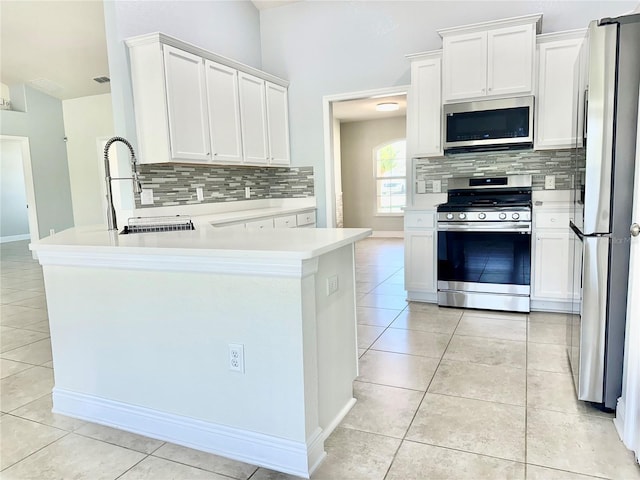 kitchen with light tile patterned floors, a peninsula, a sink, light countertops, and appliances with stainless steel finishes