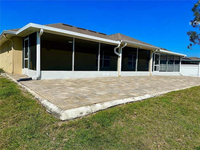 rear view of house featuring stucco siding, a patio area, a lawn, and a sunroom