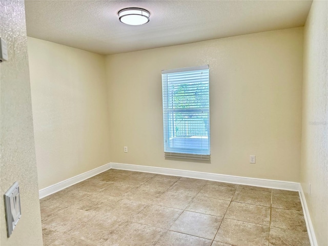 spare room with tile patterned flooring, baseboards, and a textured ceiling