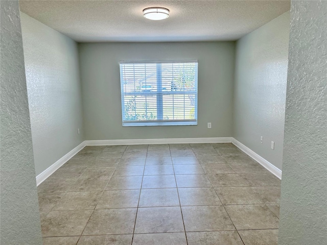 tiled empty room with a textured ceiling, baseboards, and a textured wall