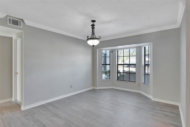 empty room with visible vents, a textured ceiling, wood finished floors, and crown molding