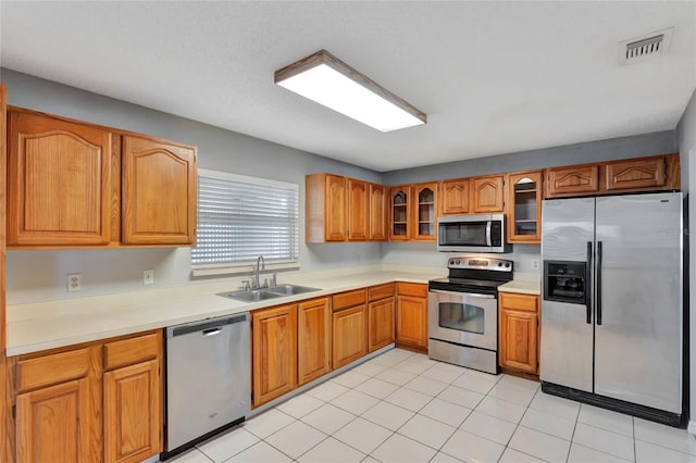 kitchen with visible vents, glass insert cabinets, brown cabinetry, stainless steel appliances, and a sink