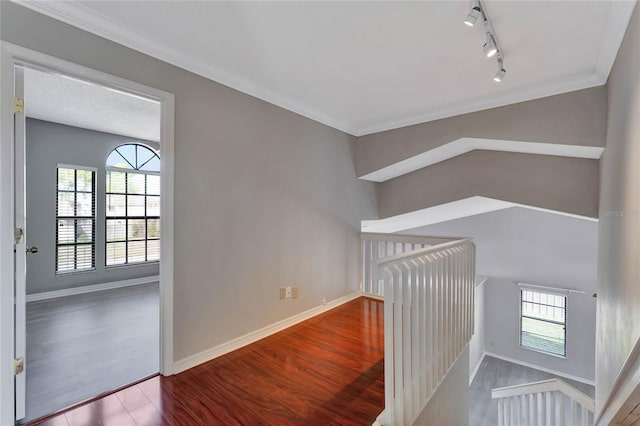 hallway with an upstairs landing, baseboards, wood finished floors, and ornamental molding