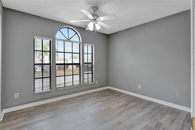 unfurnished room with ceiling fan, baseboards, a textured ceiling, and light wood-style flooring