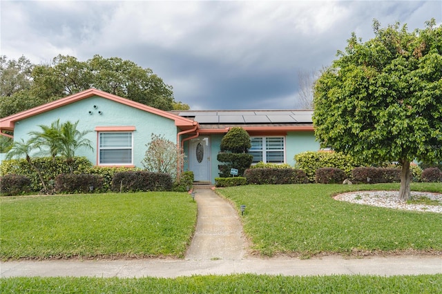 single story home featuring roof mounted solar panels, stucco siding, and a front yard