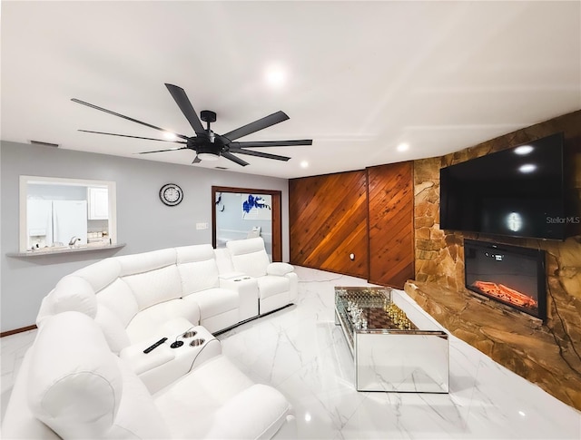 living area with visible vents, wood walls, a glass covered fireplace, marble finish floor, and a ceiling fan