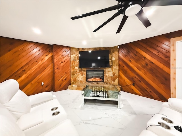 living room featuring wooden walls, a fireplace, marble finish floor, and ceiling fan