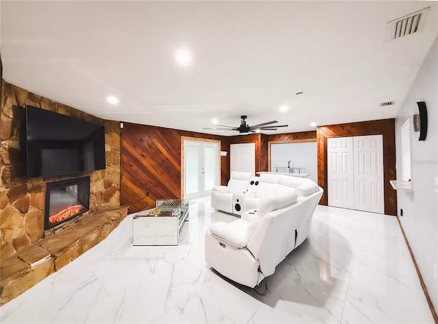 living room with visible vents, marble finish floor, a stone fireplace, and wooden walls