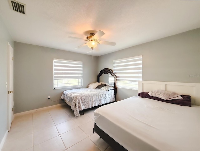 bedroom featuring multiple windows, a ceiling fan, visible vents, and light tile patterned floors