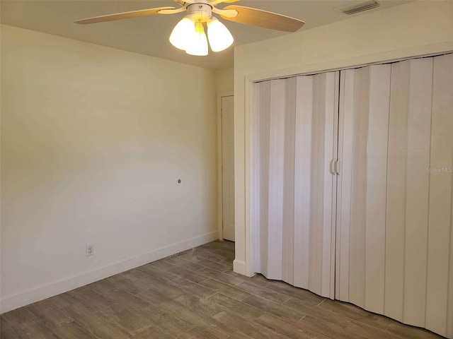unfurnished bedroom with a closet, ceiling fan, visible vents, baseboards, and wood finished floors