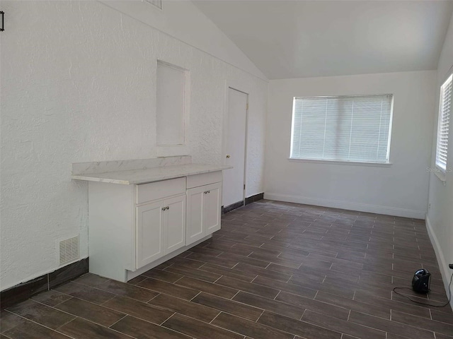spare room with dark wood-style flooring, a textured wall, lofted ceiling, and baseboards