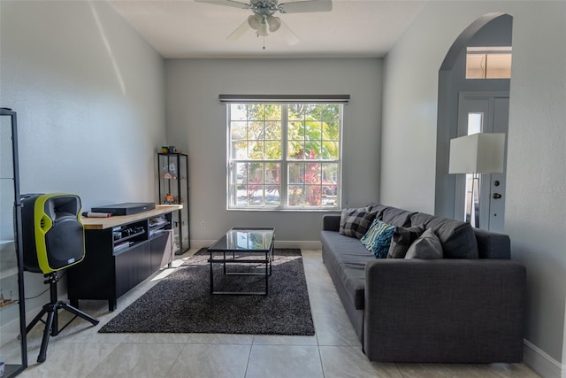 living room with light tile patterned floors, baseboards, arched walkways, and ceiling fan