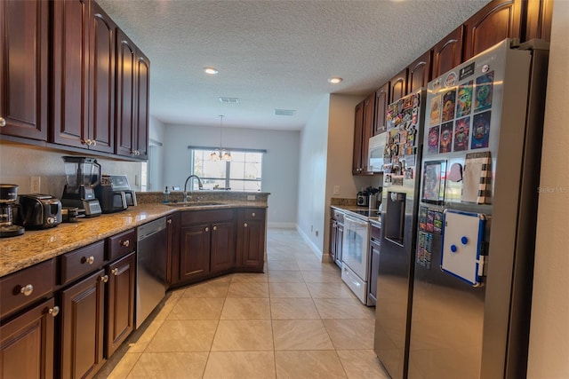 kitchen with a sink, a textured ceiling, a peninsula, appliances with stainless steel finishes, and light tile patterned flooring