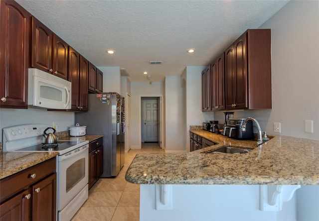 kitchen with visible vents, light stone countertops, a peninsula, white appliances, and a sink