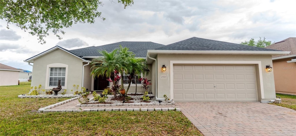 ranch-style home with stucco siding, decorative driveway, a garage, and a front lawn