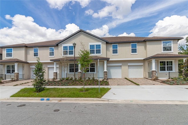 townhome / multi-family property featuring a porch, a garage, driveway, and stucco siding