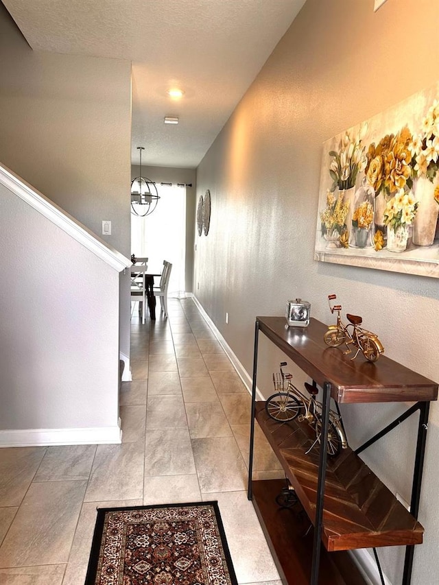 hall with baseboards, a textured ceiling, and tile patterned flooring