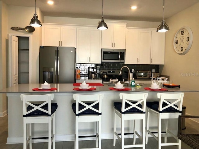 kitchen with a sink, white cabinets, appliances with stainless steel finishes, a kitchen bar, and tasteful backsplash