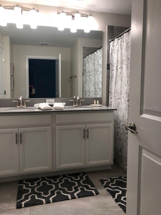 bathroom with a textured ceiling, double vanity, visible vents, and a sink
