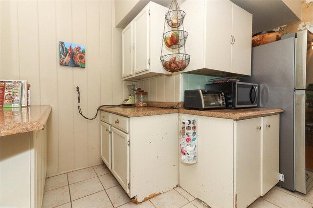 kitchen featuring stainless steel microwave, light tile patterned floors, white cabinets, and decorative backsplash
