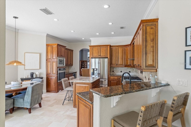 kitchen featuring visible vents, a kitchen breakfast bar, stainless steel appliances, dark stone counters, and brown cabinetry