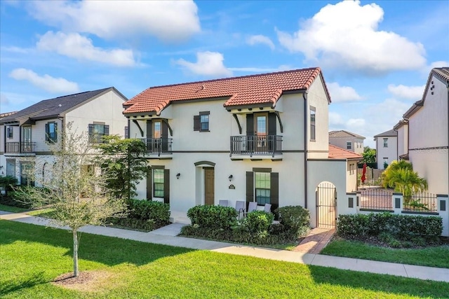 mediterranean / spanish-style house featuring a tiled roof, a front yard, stucco siding, a balcony, and a gate