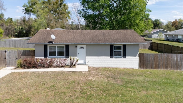 ranch-style home featuring brick siding, a front lawn, fence, roof with shingles, and stucco siding
