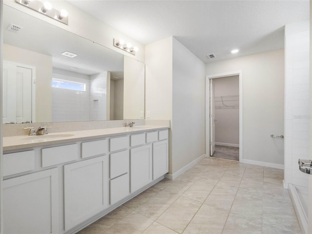 full bath featuring double vanity, a spacious closet, a tile shower, and a sink