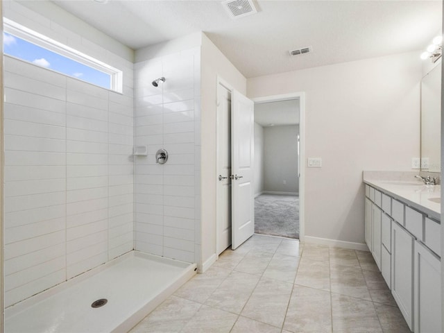 bathroom featuring double vanity, visible vents, a sink, and a tile shower