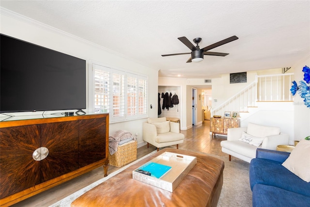 living area featuring stairway, a ceiling fan, visible vents, a textured ceiling, and crown molding