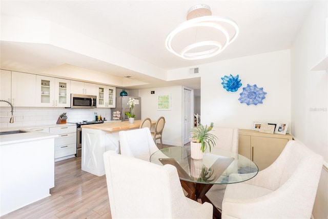 dining area featuring an inviting chandelier, a tray ceiling, visible vents, and light wood finished floors