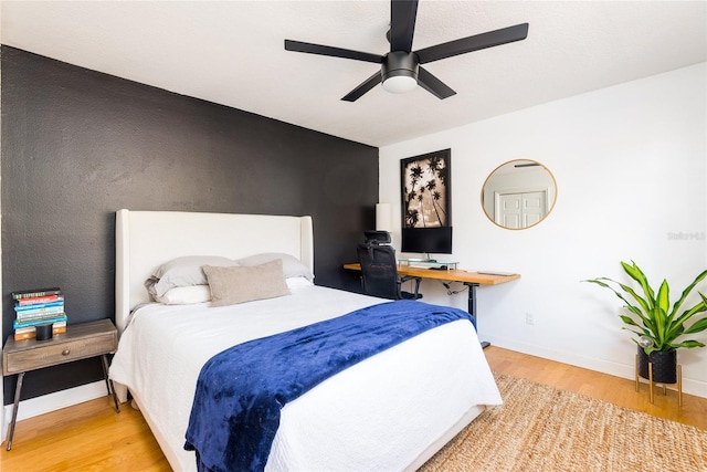 bedroom with a ceiling fan, an accent wall, baseboards, and wood finished floors