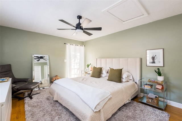 bedroom featuring a ceiling fan, attic access, wood finished floors, and baseboards