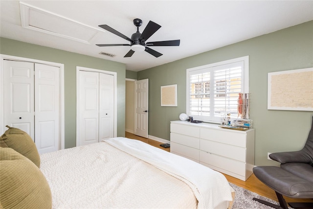 bedroom with visible vents, two closets, light wood-style flooring, attic access, and ceiling fan