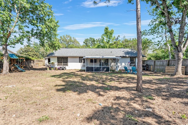 back of property featuring a sunroom, a fenced backyard, stucco siding, and a playground