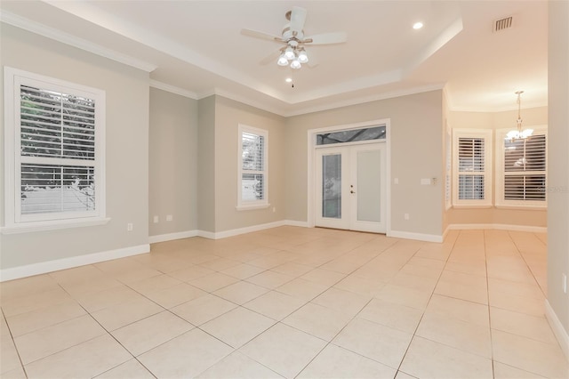 empty room with light tile patterned floors, visible vents, a tray ceiling, and ornamental molding