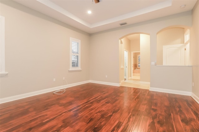 spare room with visible vents, a raised ceiling, wood finished floors, arched walkways, and baseboards