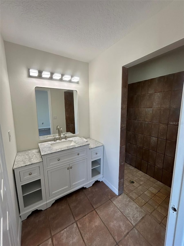 full bathroom with baseboards, a textured ceiling, vanity, and a tile shower