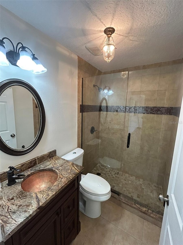 bathroom with tile patterned floors, toilet, a textured ceiling, a shower stall, and vanity